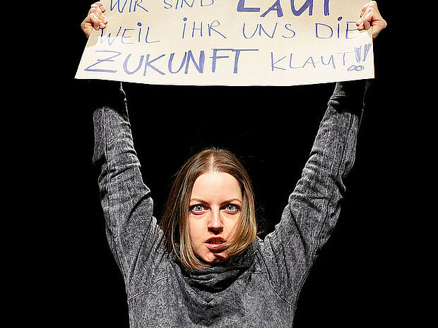 Eine junge Frau mit energischem Gesichtsausdruck hält ein Schild hoch, auf dem steht "Wir sind laut, weil ihr uns die Zukunft klaut!"